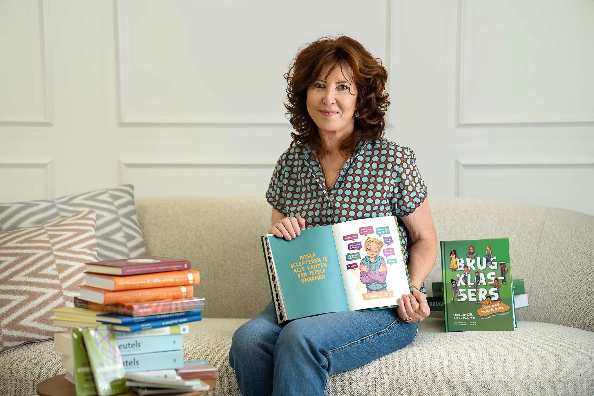 Rita Capitein met een opengeslagen exemplaar van Brugklassers, naast een stapel van haar eerdere boeken